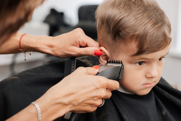 Fotografar em um salão de beleza. um barbeiro corta o cabelo de um menino com uma máquina.