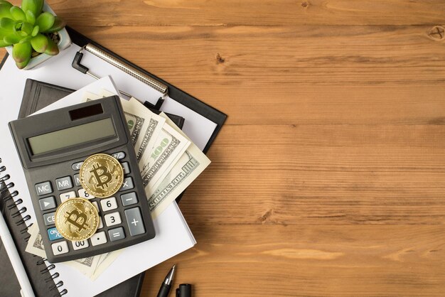 Fotografía aérea de la calculadora del portapapeles del portátil bitcoin cryptocurrency pluma negra dinero dólares y planta aislada en el fondo de madera