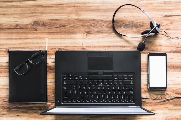 fotografía aérea de un escritorio con una computadora portátil una agenda un móvil y auriculares con un micrófono