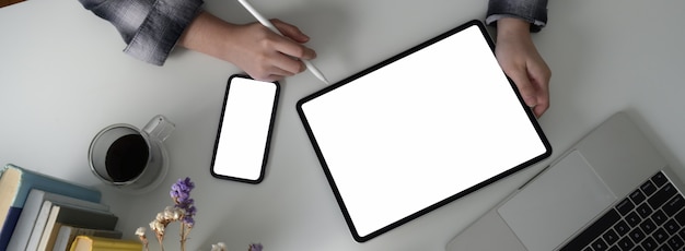 Fotografía aérea de estudiante universitaria haciendo asignación con tableta de pantalla en blanco y teléfono inteligente