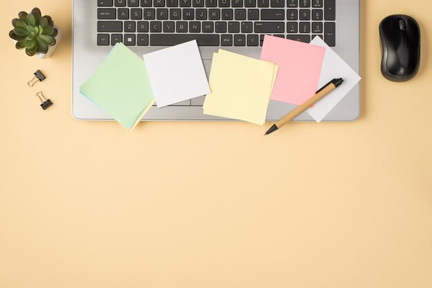 Fotografía aérea de pegatinas de colores para portátiles grises, clips, bolígrafo, ratón de ordenador y planta aislada en el fondo beige con espacio de copia