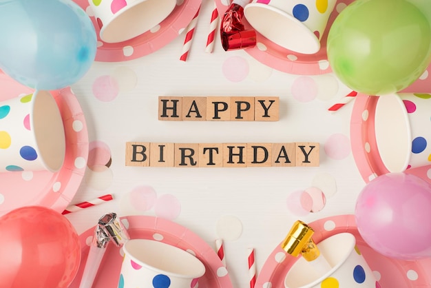 Fotografía aérea de tazas, platos, túbulos de fiesta, silbato y globos con inscripción feliz cumpleaños aislado en el fondo blanco.