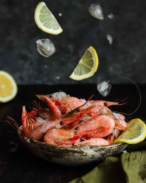 Fotografía de alimentos de levitación con gambas, hielo y limón Fotografía Lowkey sobre un fondo oscuro