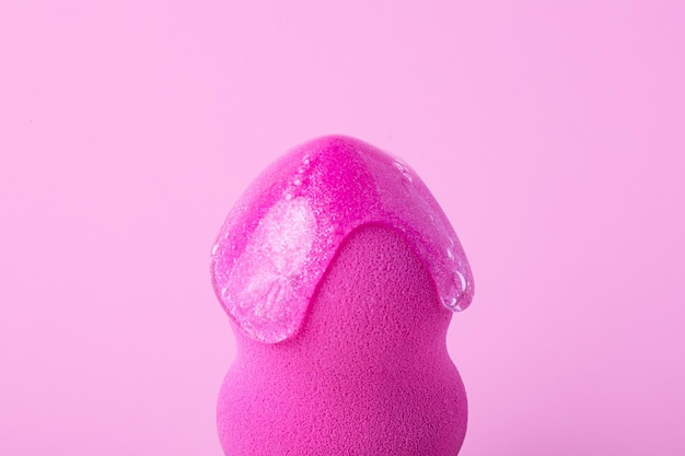 Fotografia aproximada de beauty blender com gotejamento de gel cosmético sobre fundo rosa de framboesa