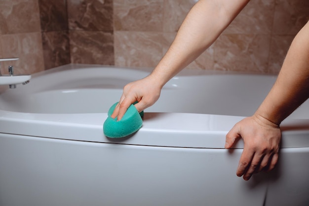 Una fotografía aproximada de las manos de un hombre limpiando un baño de cerámica blanca con una esponja azul El concepto de limpieza