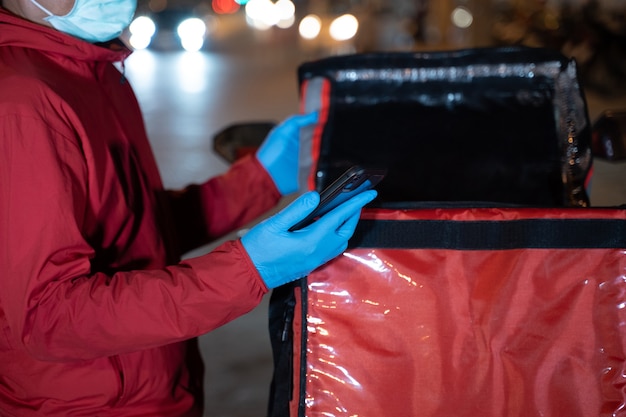 Fotografía de archivo de un repartidor de alimentos en uniforme rojo que lleva una caja de entrega de alimentos para entregar al cliente para su pedido durante la pandemia de COVID-19 y el cierre en la ciudad por la noche en Tailandia.