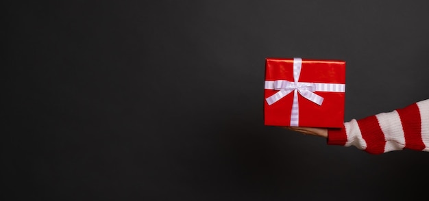 Fotografía de banner de la mano femenina con caja de regalo roja aislada sobre fondo gris