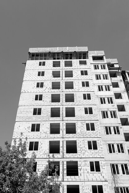 Fotografía en blanco y negro de un edificio residencial de varios pisos en construcción y grúa sobre un fondo de cielo azul