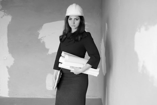 Fotografía en blanco y negro de una mujer arquitecta en el sitio de construcción con dibujos y cuaderno