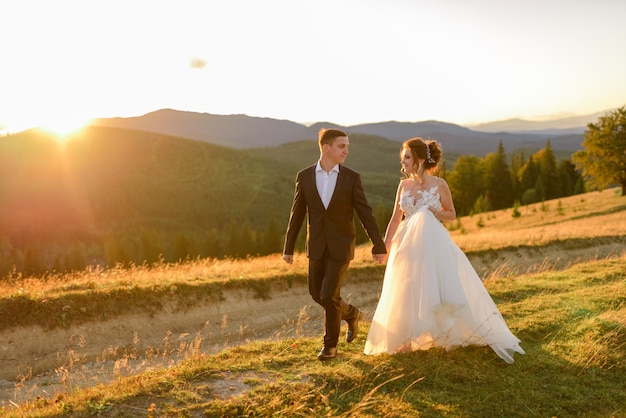 Fotografía de bodas en las montañas. La novia y el novio se toman de la mano y caminan al atardecer.