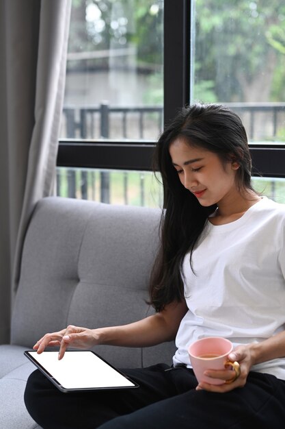 Fotografía cenital de casual joven sentado en el sofá en la sala de estar con teléfono inteligente y tomando café.