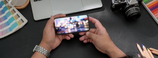 Fotografía cenital del fotógrafo mirando un video en un teléfono inteligente horizontal en un espacio de trabajo moderno y oscuro