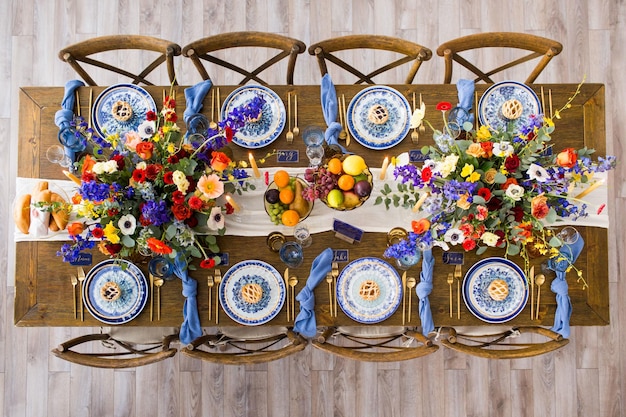 Fotografía cenital de una mesa y sillas de madera decoradas con flores, velas, tazones de fruta, etc.