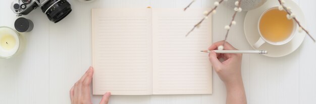 Fotografía cenital de una mujer escribiendo en el cuaderno diario en blanco sobre la mesa de tablones