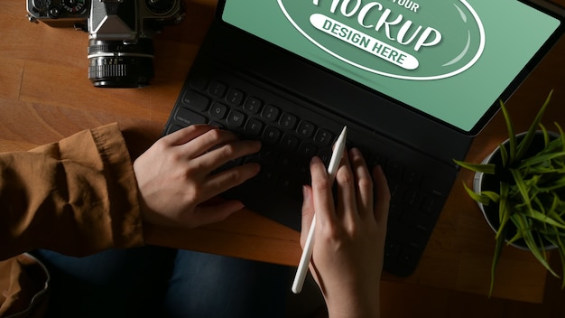 Foto fotografía cenital de mujer escribiendo en el teclado de la tableta simulada mientras sostiene el lápiz óptico en la mesa de madera