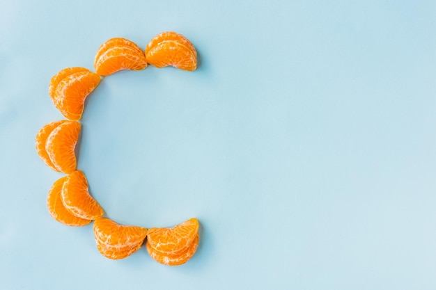 Fotografía cenital de rodajas de naranja formando letras C sobre un fondo azul claro