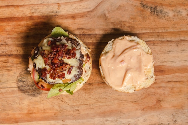 Fotografía cenital de una sabrosa hamburguesa dividida por la mitad encima de una mesa de madera con fondo negro.