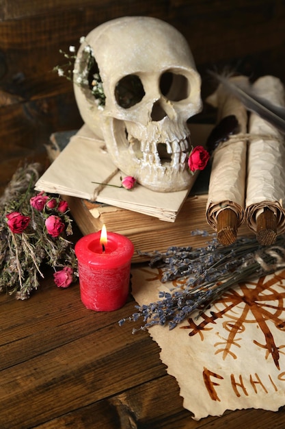 Fotografía conceptual de la composición mágica del amor con el cráneo de la muñeca vudú, hierbas secas y velas sobre fondo de madera oscura.