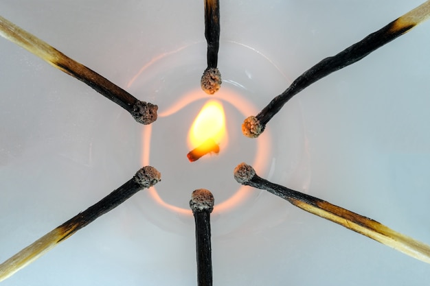 Fotografía conceptual de una vela encendida con fósforos quemados alrededor de una mecha encendida de cerca