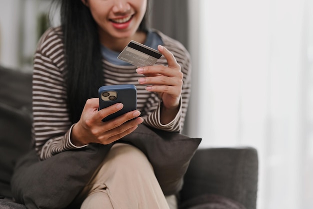 Foto fotografia cortada de uma jovem sorridente segurando um cartão de crédito e um smartphone pagando on-line encomendando na internet