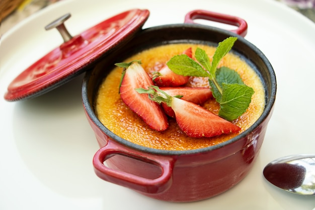 Fotografia da vista de cima da sobremesa creme brulee decorada com hortelã fresca e morango