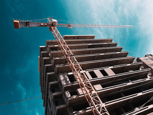 Foto fotografia de baixo ângulo de um guindaste por um edifício inacabado em um canteiro de obras