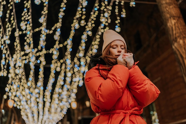 Fotografia de baixo de uma jovem congelada com chapéu e casaco de inverno a aquecer as mãos no inverno frio