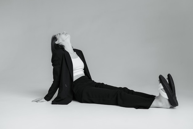 Fotografia de moda de uma mulher elegante em terno preto sentada no chão do estúdio