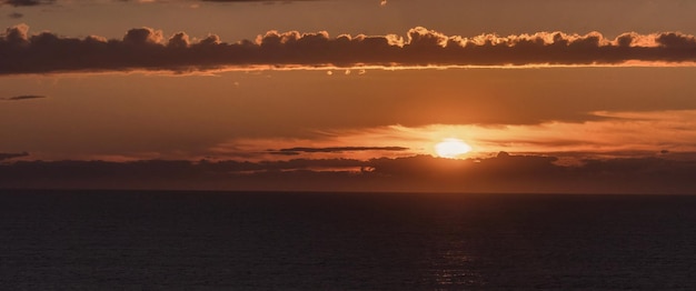 Fotografia do nascer do sol na costa com o sol e as nuvens ao fundo