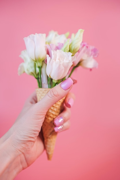 Fotografia em close-up de uma mulher com a mão segurando um cone de waffle com flores cor-de-rosa e brancas