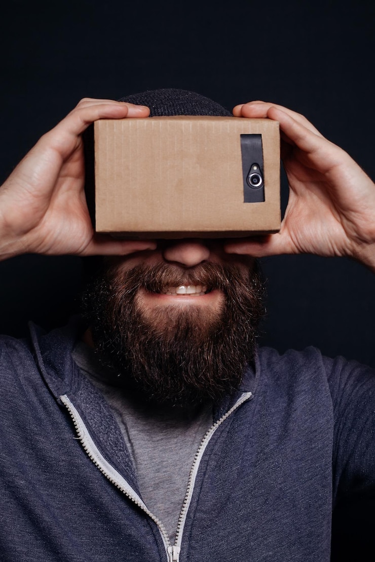 Foto fotografia em cores de um jovem olhando através de um tabuleiro de cartas um dispositivo com o qual se pode experimentar a realidade virtual em um telefone móvel um cara sorrindo
