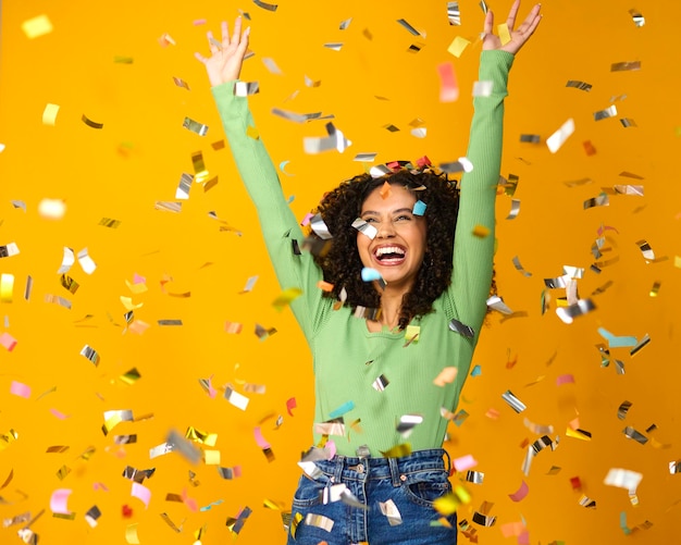 Fotografía de estudio de una mujer emocionada celebrando una gran victoria bañada en confeti de oropel sobre un fondo amarillo
