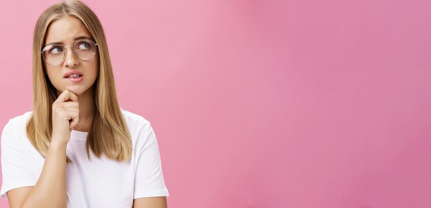 Fotografía de estudio de una mujer insegura, inteligente y nerd con gafas y camiseta blanca de pie preocupada y preocupada.