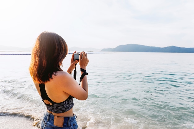 Fotografía femenina con cámara tomando una foto del mar.