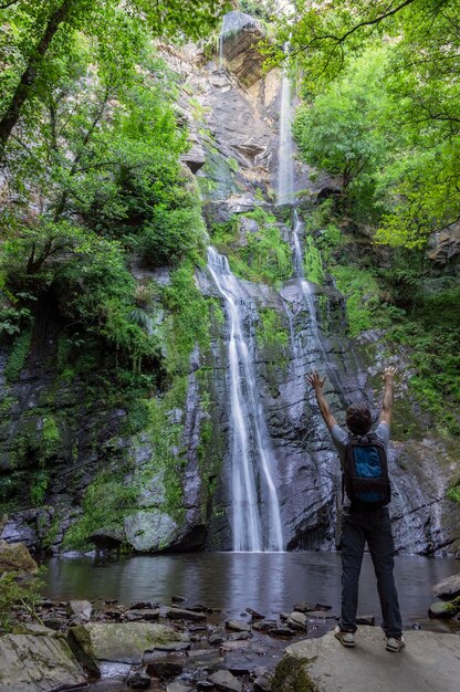 Fotografía en formato vertical de un joven contemplando una cascada entre los árboles, Lugo