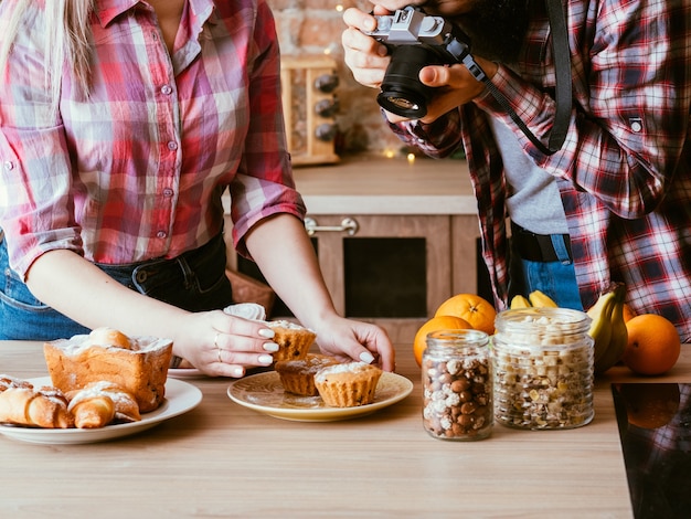 Fotografía gastronómica. Panadería dulce. Hombre y mujer tomando fotos de muffins caseros. Pasteles frescos, frascos con nueces y frutas alrededor.