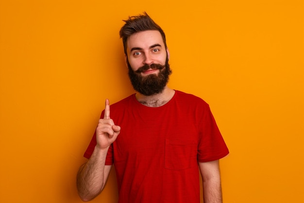 Fotografía gratuita en interiores de una persona positiva con una camiseta roja casual con el dedo índice a un lado