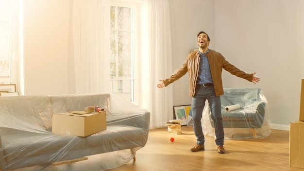 Foto fotografía de un hombre muy feliz que se muda a su nuevo apartamento y posa a un tipo emocionado que compró una nueva casa listo para comenzar a desempacar cajas de cartón