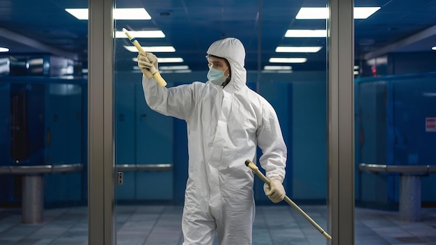 Fotografía de un hombre con un traje blanco de protección química desinfectando áreas públicas para detener el esp.