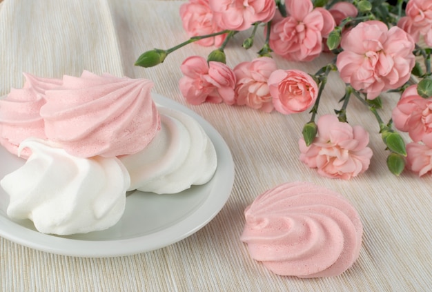 Foto fotografía macro de galletas de merengue blanco y rosa hechas de claras de huevo batidas y azúcar de cerca. merengues batidos tradicionales, crema batida horneada o beze con flores de clavel rosa