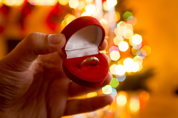 Fotografía macro del hombre que presenta el anillo de oro en la caja contra el árbol de Navidad decorado