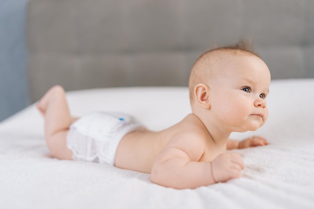 Fotografia média de um bebê doce vestindo fraldas brancas deitado de barriga e felizmente agitando os braços e