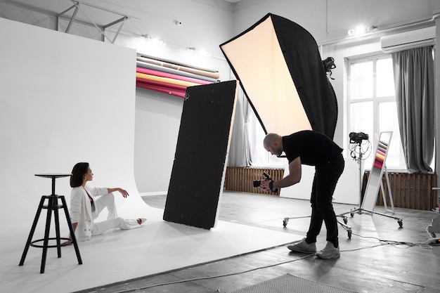 Fotografía de moda en un estudio fotográfico. Fotógrafo profesional masculino tomando fotografías de la hermosa modelo de mujer en la cámara, entre bastidores