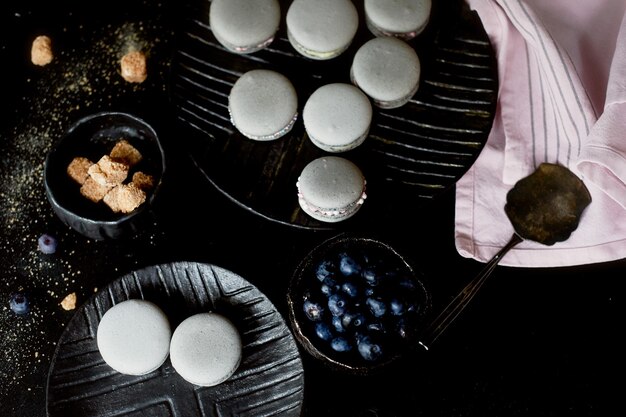 Fotografia monocromática escura Macaroons de bolos cinza na superfície escura da mesa ao lado de uma colher e açucareiro com açúcar mascavoE toalhas rosa de pano simples