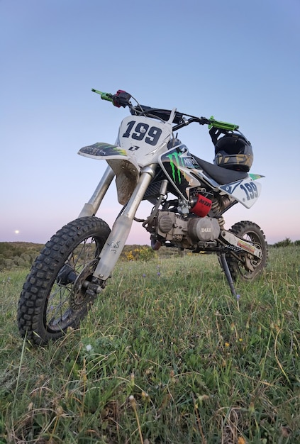 fotografía de motocross pit bike en campo verde con cielo azul y casco negro y dorado