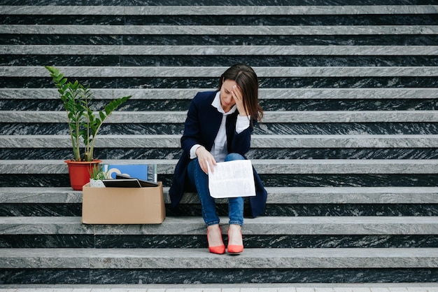 La fotografía muestra a una oficinista angustiada y molesta sentada en una escalera al aire libre.