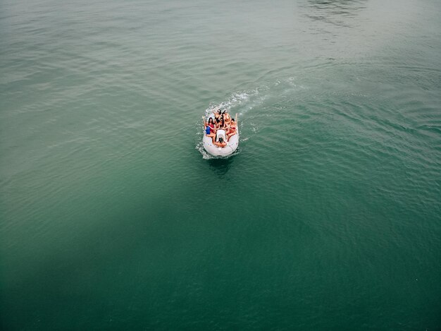 Fotografía de naturaleza turística desde un helicóptero. Un chico joven toma fotos de chicas lindas en trajes de baño y gafas de sol. Levantando manos. Foto de lujo en un barco a motor en alta mar.
