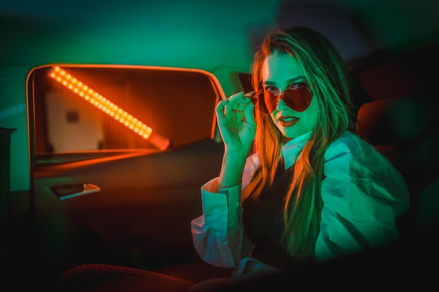 Fotografía de neón dentro de un auto de una joven rubia con gafas de corazón