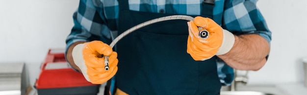Foto fotografía panorámica de un reparador con guantes de goma sosteniendo una manguera de metal