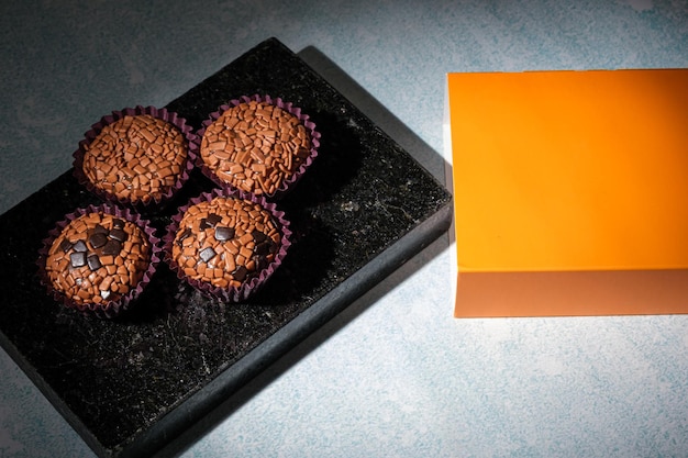 Fotografía de bajo perfil Brigadeiros dispuesta sobre una piedra de mármol negro brillante junto a una caja naranja